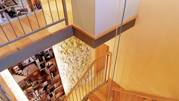 A multi-level interior with wooden staircases and a view of a lower level with various rooms and furniture. - Urbi Apartments (Manresa)