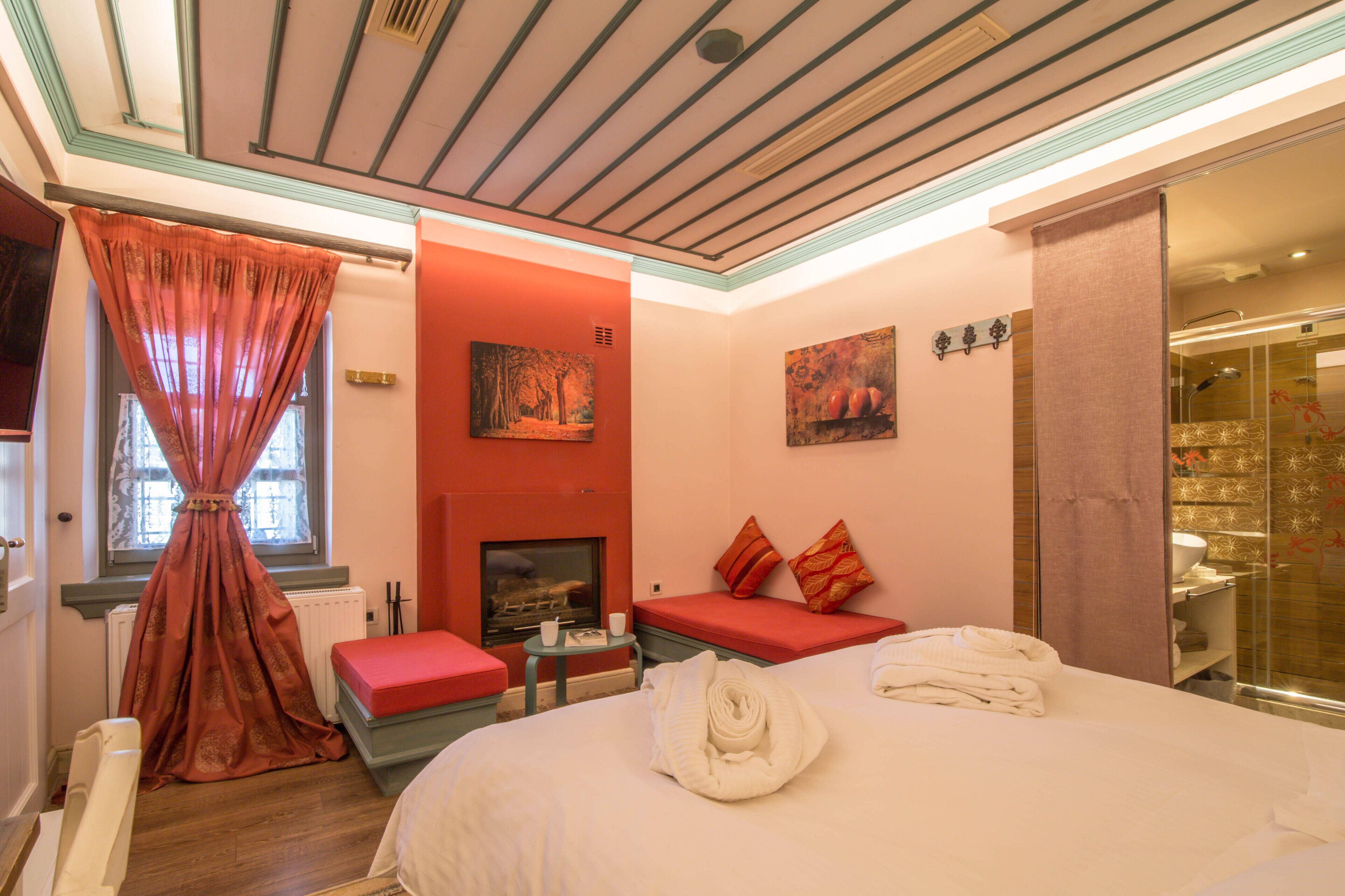 Une chambre d’hôtel avec un grand lit, une petite table avec une tasse et une soucoupe, un banc rouge, une cheminée et une douche en verre.