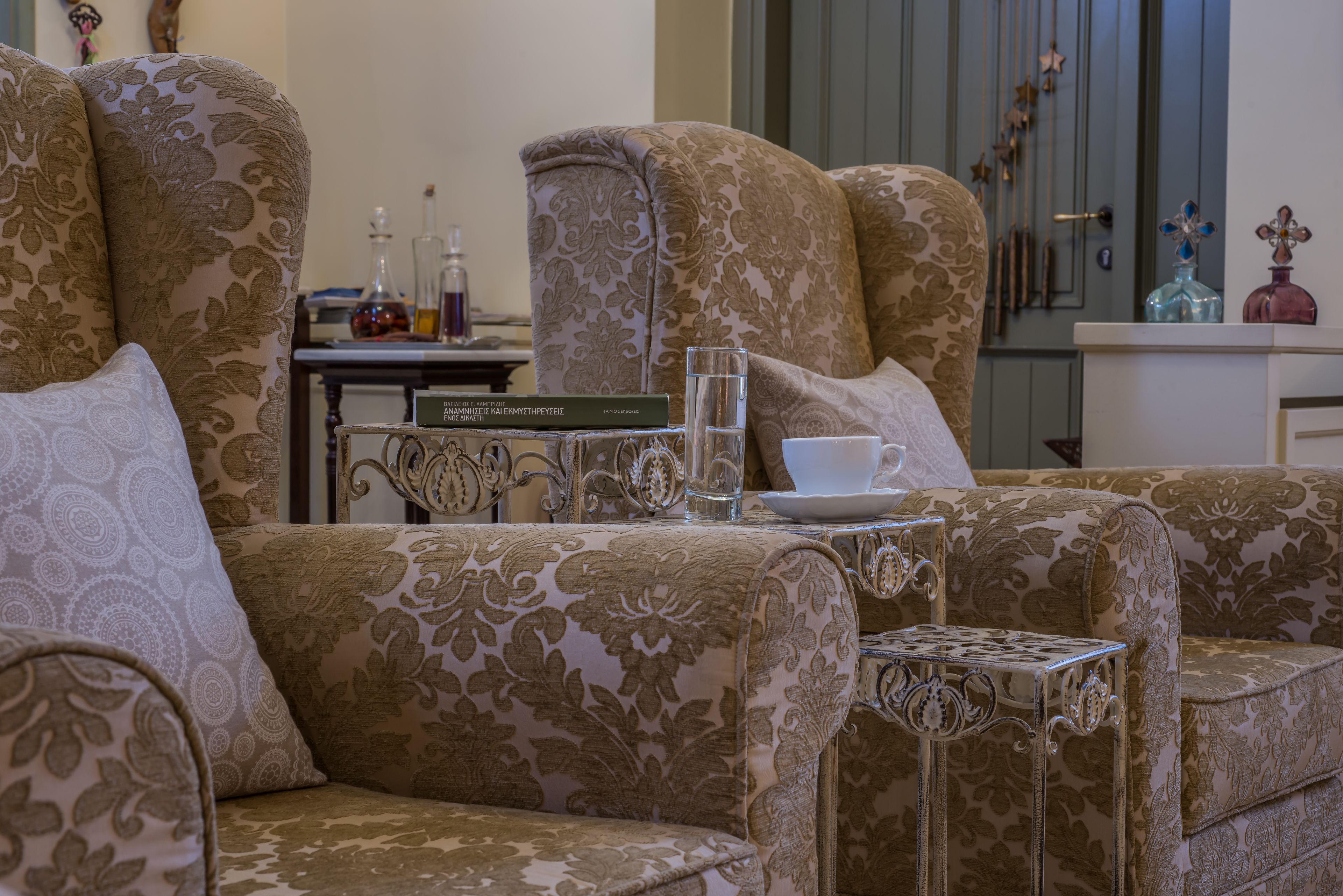 A room with a patterned sofa set, a small table with a glass and a book, and decorative items on a cabinet.