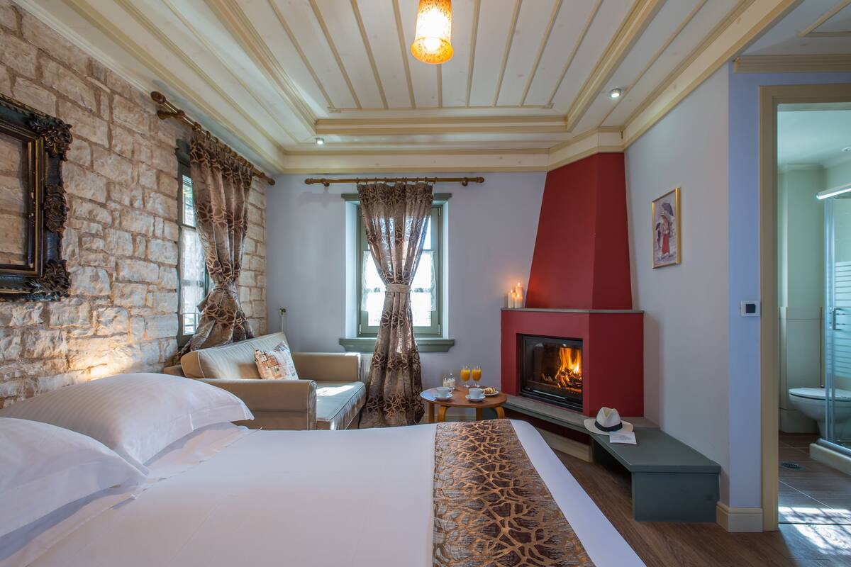 Een hotelkamer met een open haard, een bed met witte lakens, een stenen muur en een rode accentmuur.