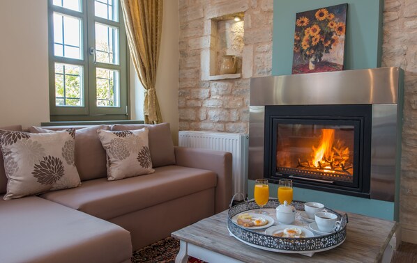 Un salon chaleureux avec un mur en pierre, une cheminée, un canapé agrémenté de coussins décoratifs et un plateau contenant des éléments pour le petit-déjeuner.