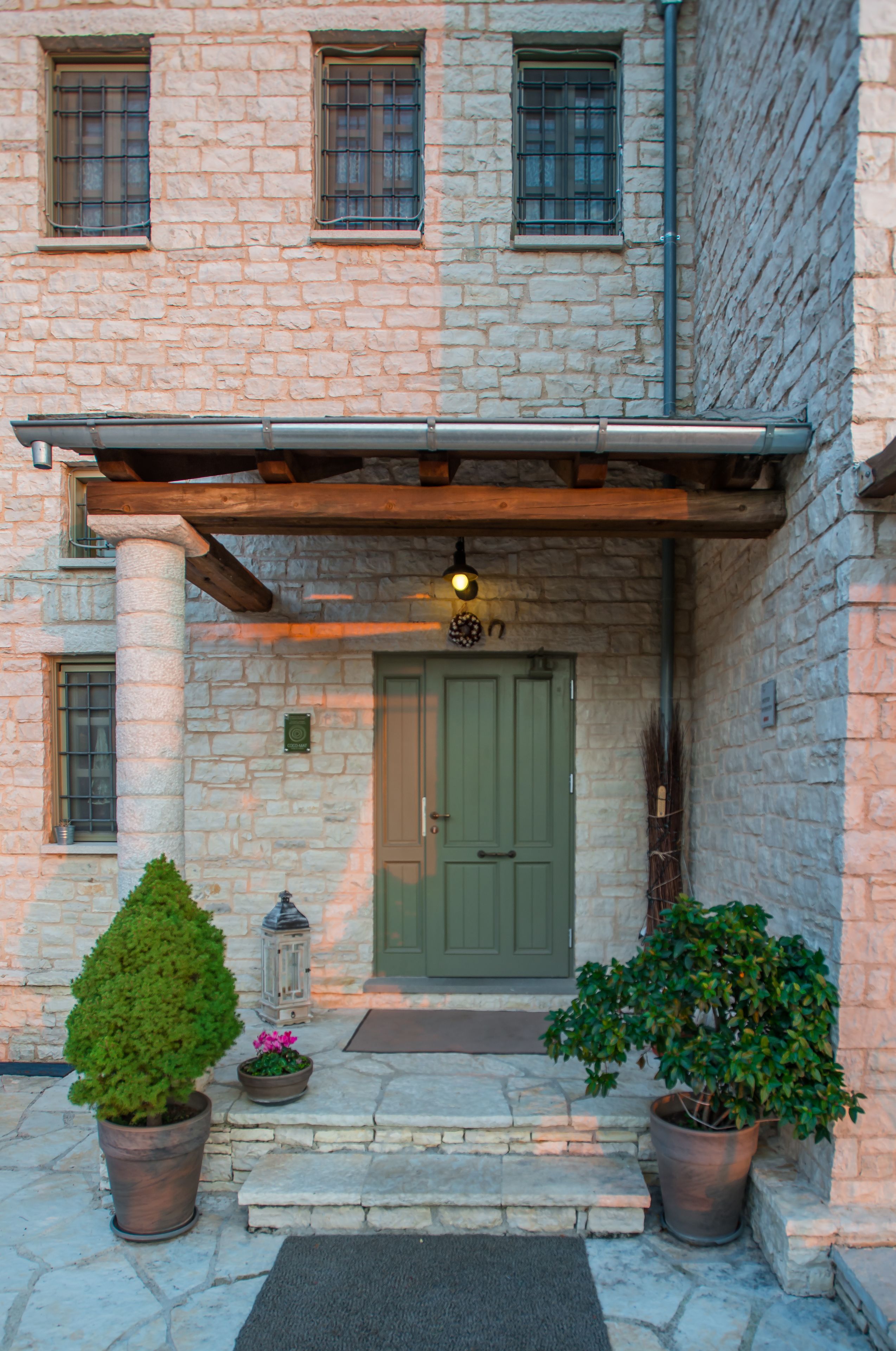 A stone building with a green door, potted plants, and a lantern.