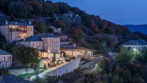 Un bâtiment en pierre doté de nombreuses fenêtres et d’un balcon, entouré d’arbres et de collines.