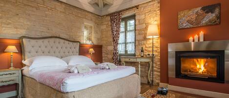 Un dormitorio con pared de piedra, chimenea, cama con cabecera, lámparas de noche y mesita de noche.