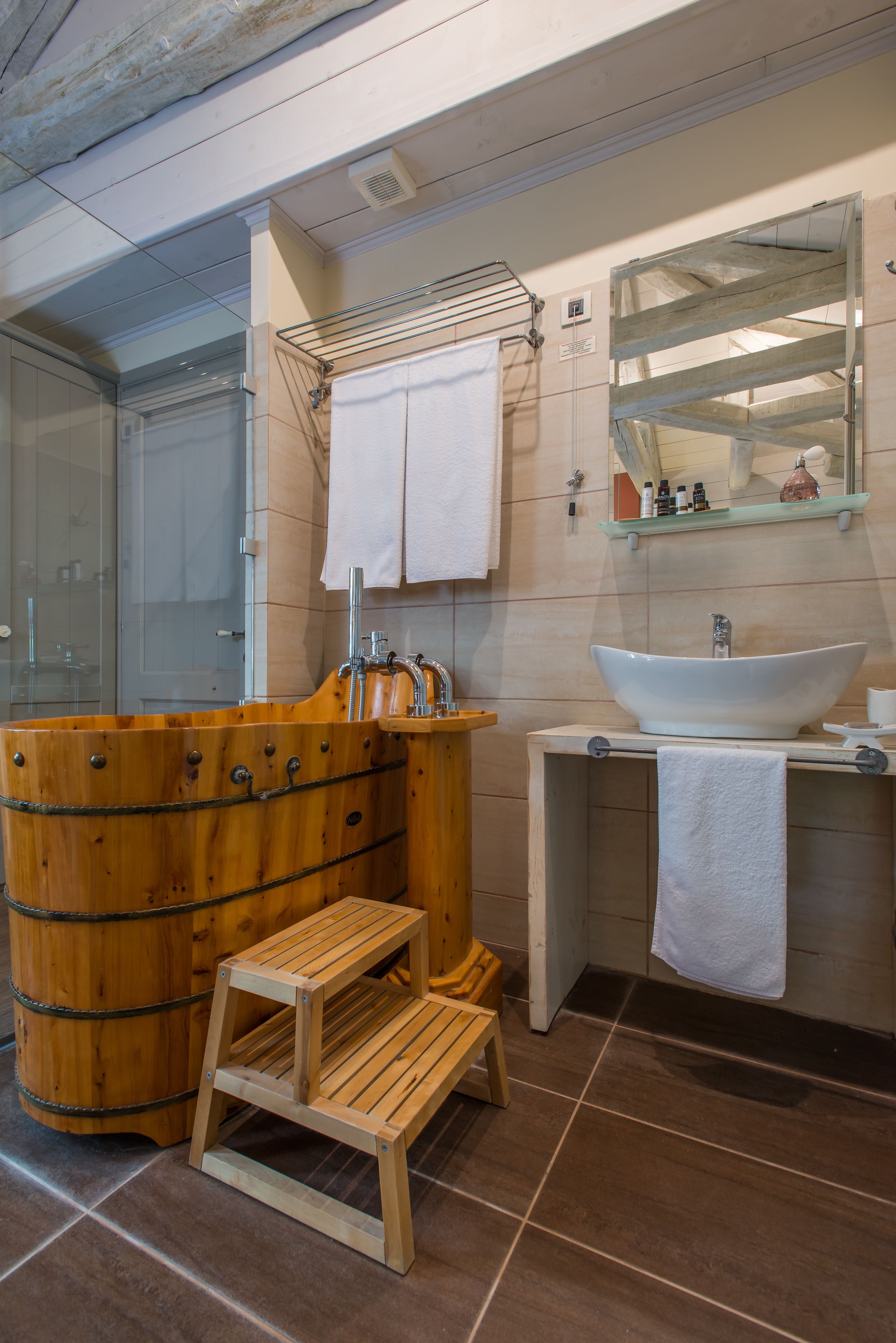 Un baño moderno con una bañera de madera, ducha con cerramiento de vidrio y un lavamanos grande con espejo arriba.