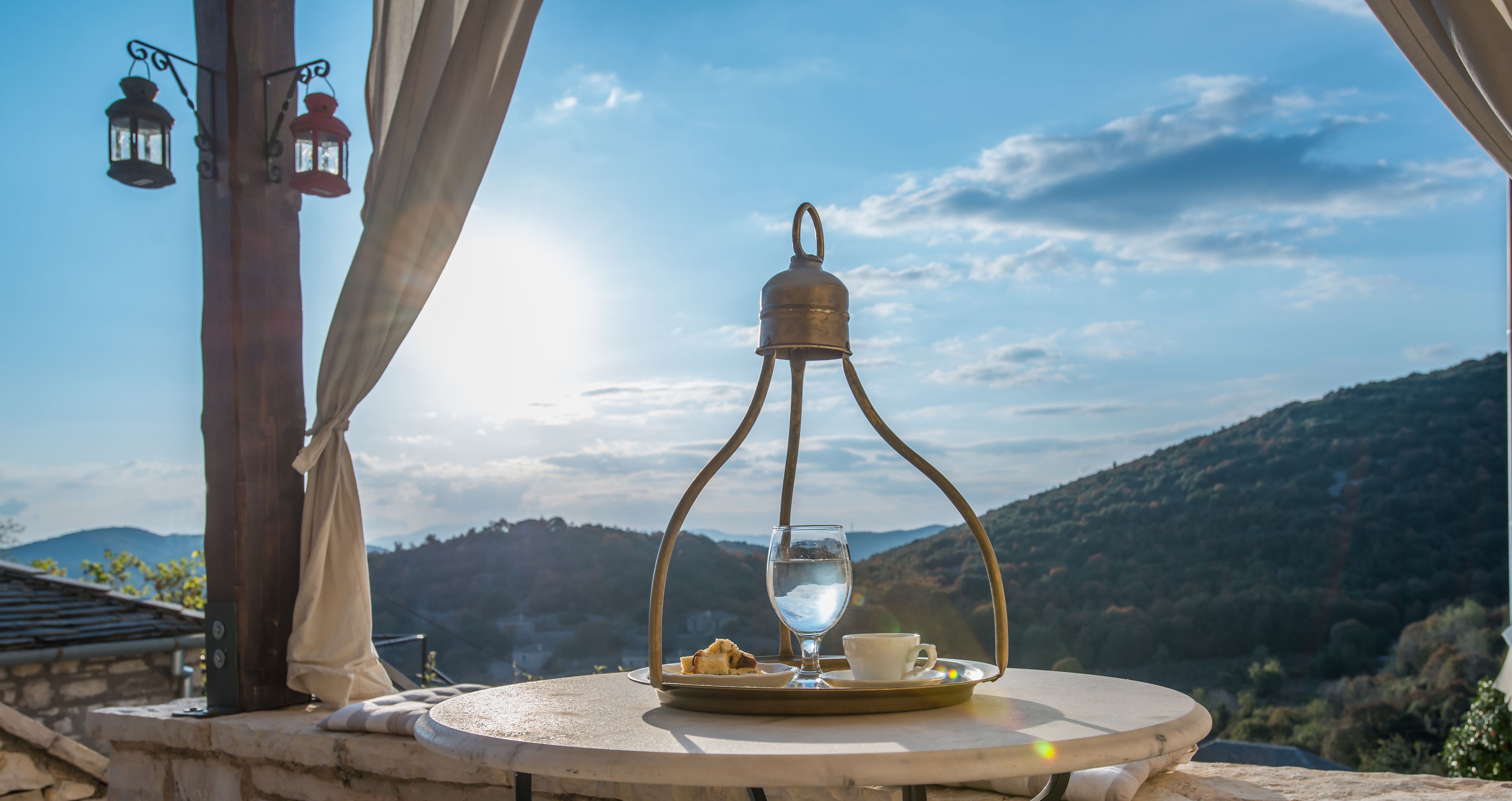 Mesa com bule, xícara e prato, com paisagem de montanhas ao fundo.