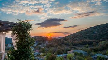 A sunset view from a balcony with a pergola, potted plants, and a stone wall.