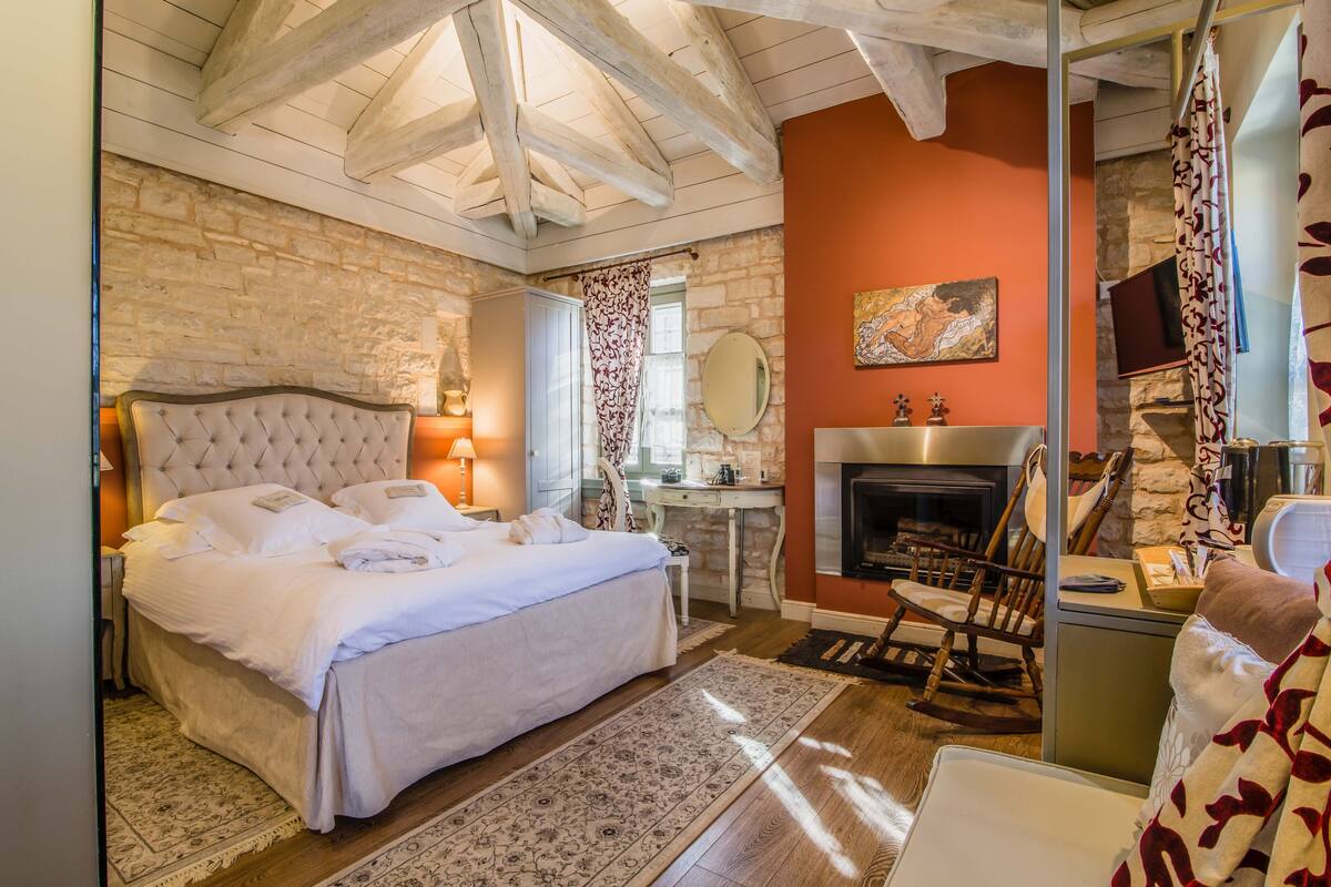 Een slaapkamer met een groot bed, een stenen muur, een open haard en een houten plafond.