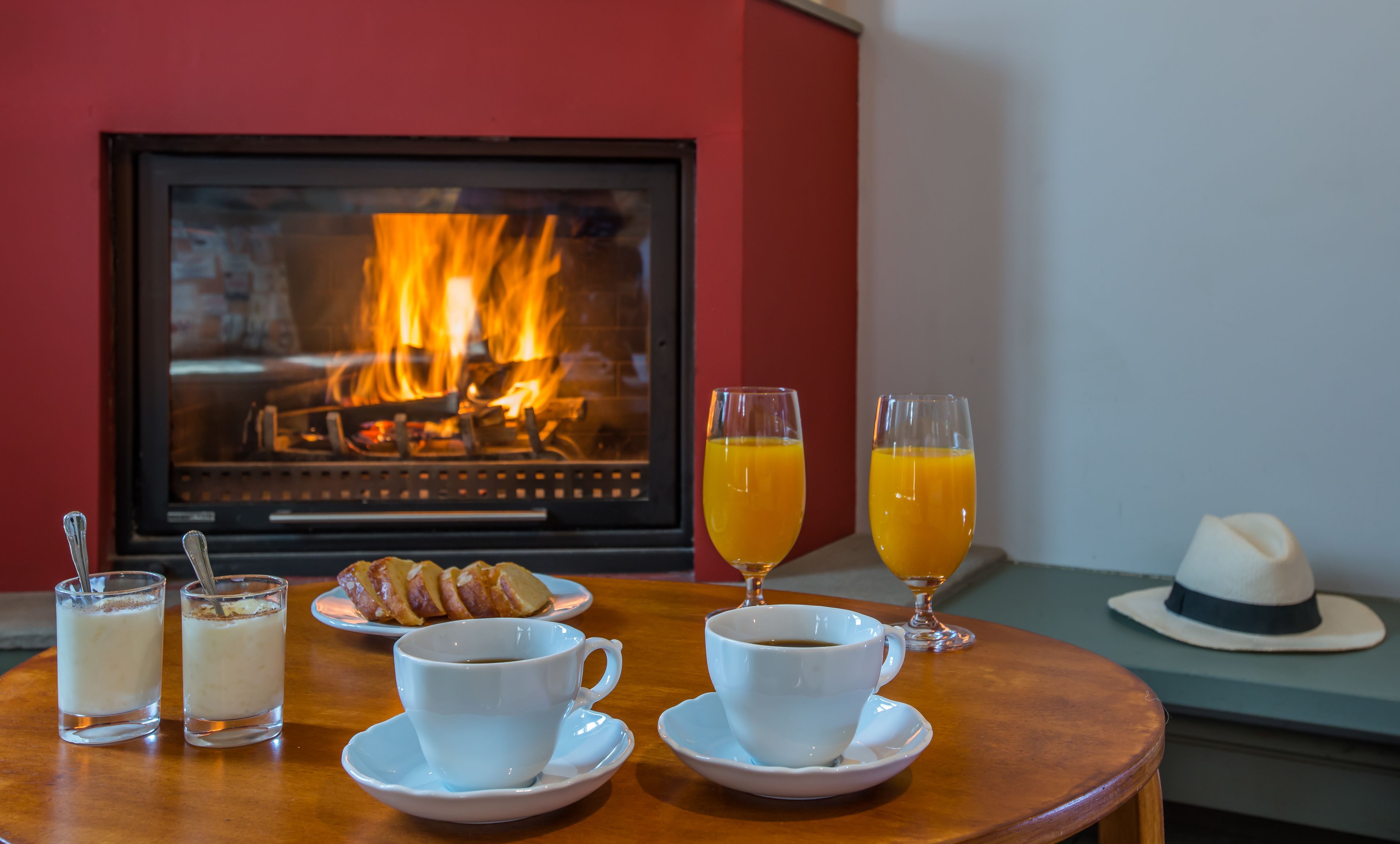 Ein gemütliches Frühstück mit Kamin, einem Tisch mit Croissants, Kaffee und Orangensaft.