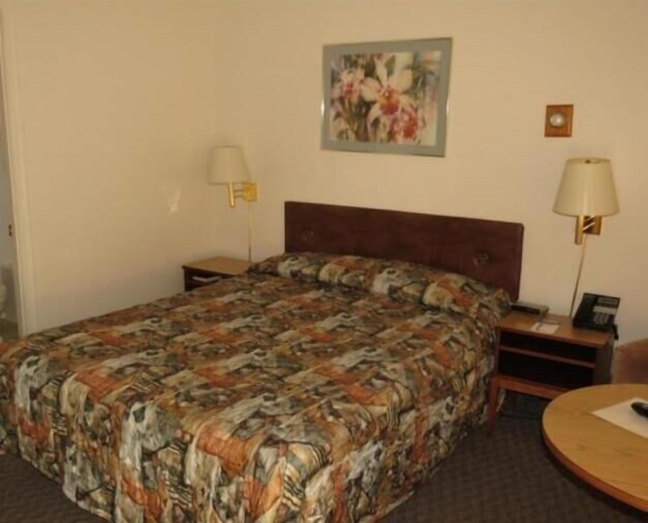 A hotel room with a large bed, two bedside tables, a round table, a lamp, and a painting on the wall.