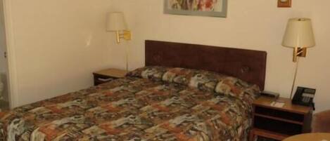 Habitación de hotel con una cama grande, dos mesitas de noche, una mesa redonda, una lámpara y un cuadro en la pared.