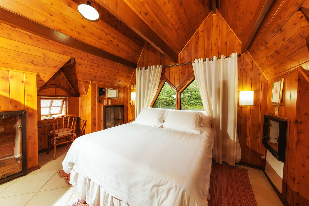 A wooden cabin bedroom with a large bed, a wooden desk, and a fireplace.