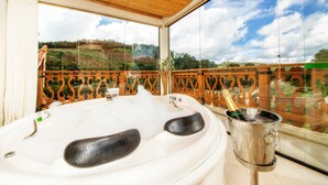 Un jacuzzi con una botella de champán, un balcón con vistas a un paisaje montañoso y un techo de madera.
