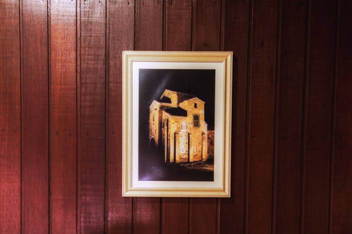 A hotel room with a wooden wall, a framed picture of a building, and a bed with white linens.