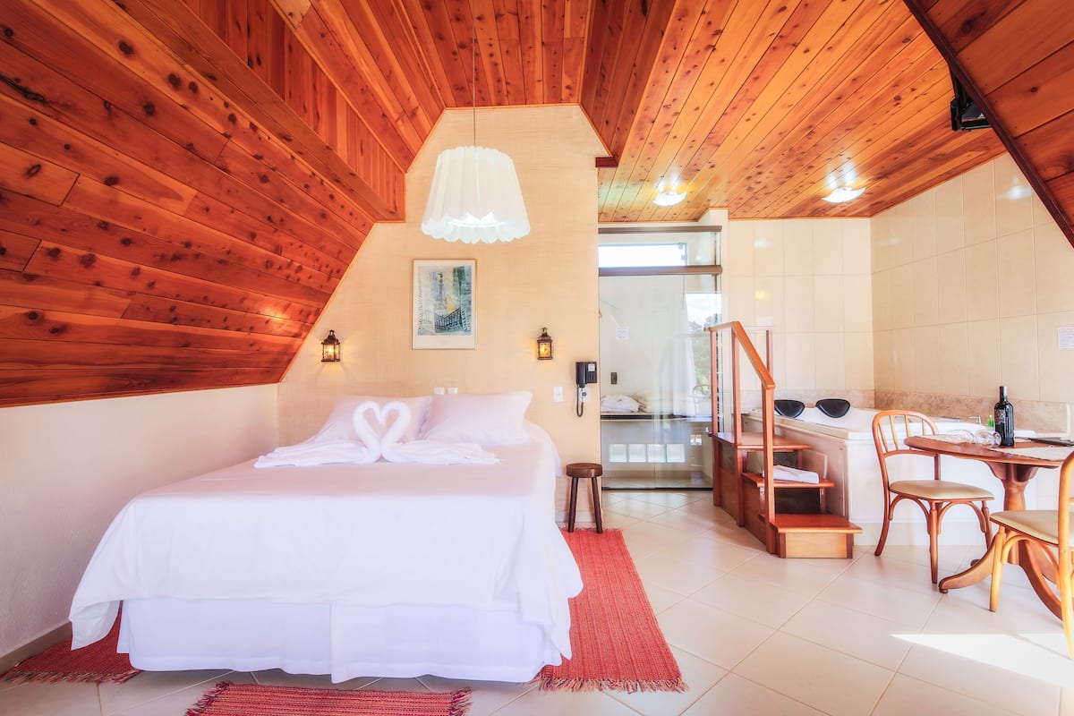 A bedroom with a large bed, wooden ceiling, a small stool, a desk, and a chair.