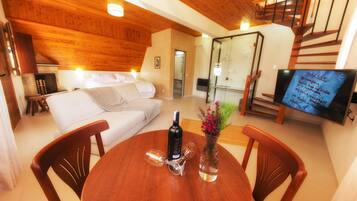Una sala de estar acogedora con techo de madera, un sofá, una mesa de comedor con sillas, una chimenea y un televisor mostrando una lista.