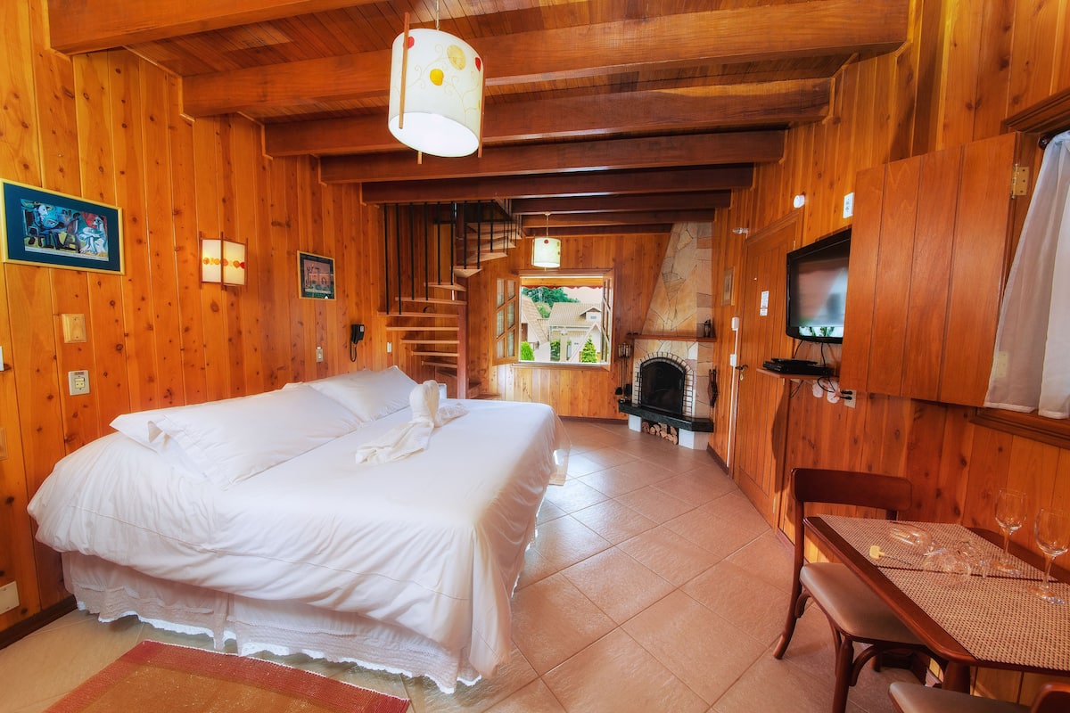 A wooden room with a bed, a table with glasses, and a TV.