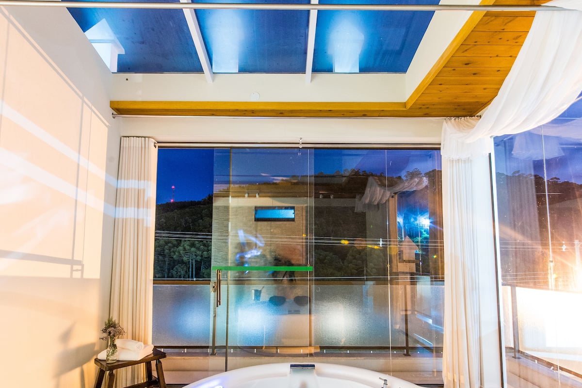 A modern indoor pool area with a glass-enclosed space, a hot tub, and a view of the outside.