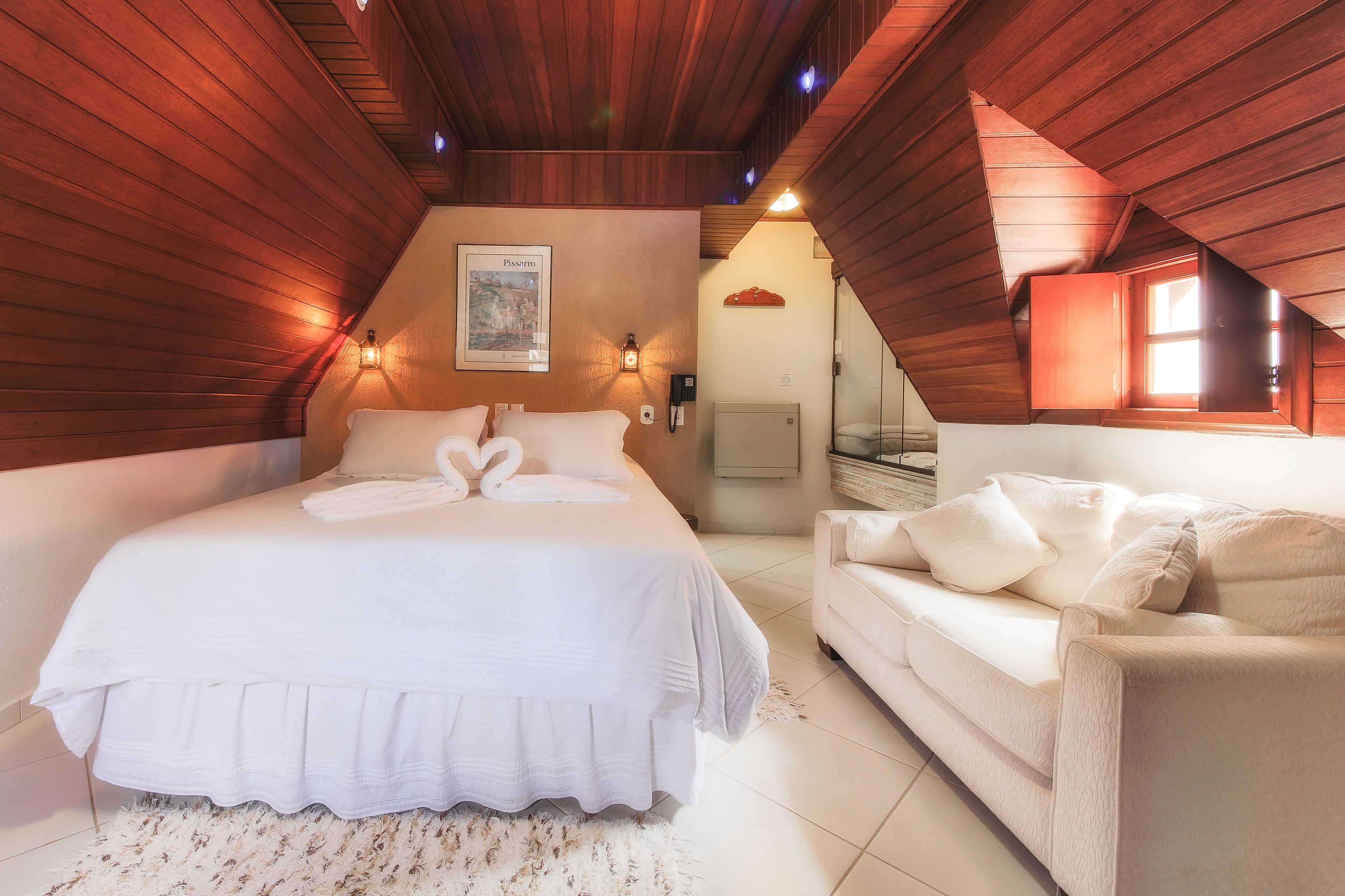 A bedroom with a large bed, a sofa, wooden ceiling beams, and a framed picture on the wall.