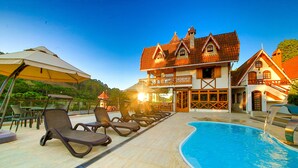 Zona junto a la piscina con sillones de descanso, una piscina y un edificio tradicional con balcón.