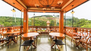 Terraza de madera con mesas y sillas redondas, con vistas a un paisaje verde exuberante y una pequeña pagoda.