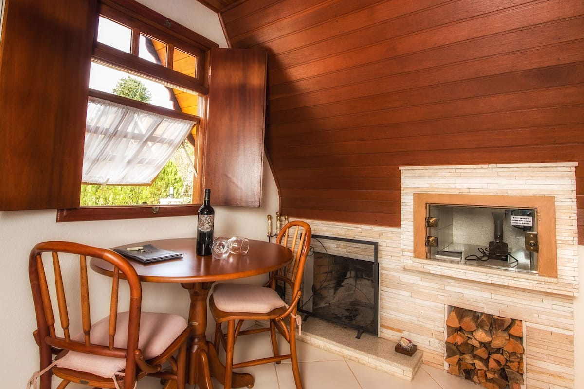 A wooden-paneled room with a dining table, chairs, a fireplace, and a window with curtains.