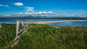 A coastal landscape with a wooden fence, grassy foreground, and a view of the sea and distant mountains under a clear sky. - Shallow Bay Motel & Cabins (Cow Head)