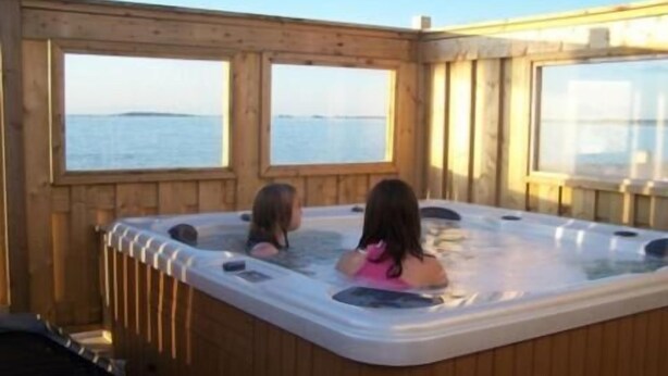 A wooden cabin with a hot tub and a view of the water. - Shallow Bay Motel & Cabins (Cow Head)