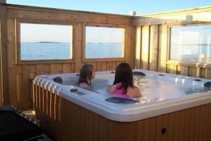 A wooden cabin with a hot tub and a view of the water.