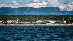 A coastal building complex with multiple structures, a rocky shoreline, and a backdrop of mountains. - Shallow Bay Motel & Cabins (Cow Head)