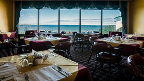 A dining area with tables set for service, large windows with a view of the sea, and a patterned carpet. - Shallow Bay Motel & Cabins (Cow Head)