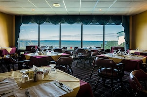 A dining area with tables set for service, large windows with a view of the sea, and a patterned carpet.
