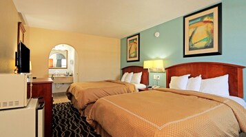A hotel room with two beds, a desk, a mirror, and artwork on the walls.