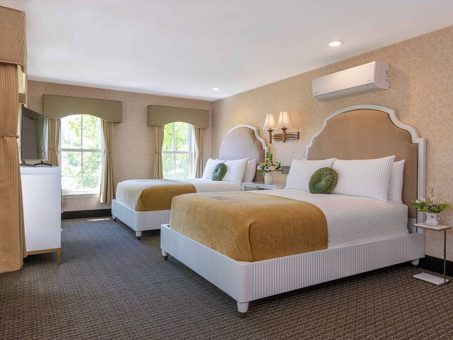 A hotel room with two beds, a large window, a mirror, a bedside table, and a wall-mounted air conditioner.