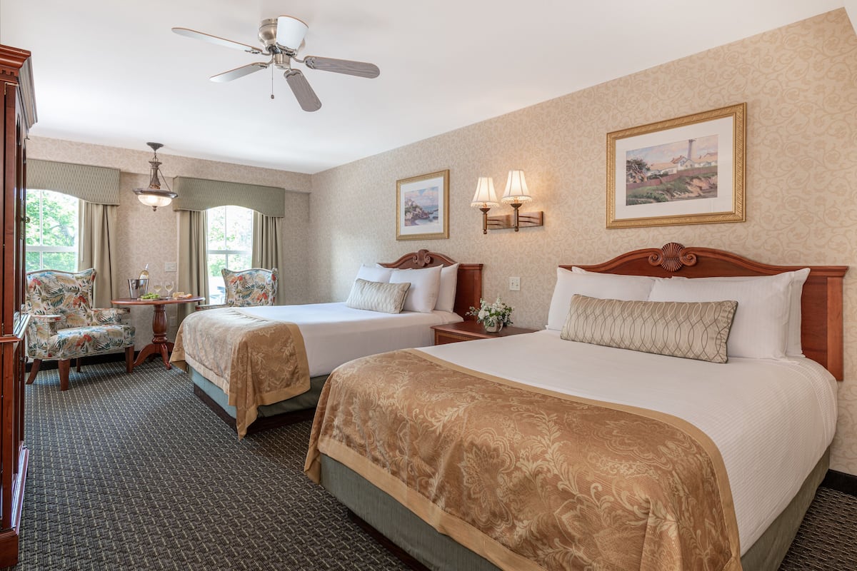 A hotel room with two beds, a ceiling fan, a desk with a chair, and two wall-mounted lamps.