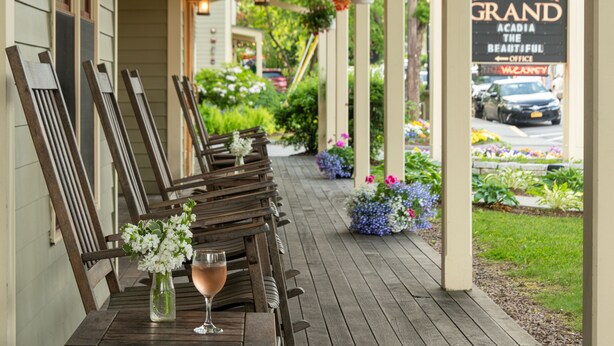 A wooden outdoor seating area with chairs and a table, a flower vase, and a sign for Bar Harbor Grand. - Bar Harbor Grand Hotel (Bar Harbor)