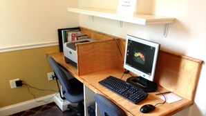 A wooden desk with a computer, keyboard, and mouse. There is a chair, a printer, and a shelf with books. - Bar Harbor Grand Hotel (Bar Harbor)