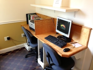 A wooden desk with a computer, keyboard, and mouse. There is a chair, a printer, and a shelf with books. - Bar Harbor Grand Hotel (Bar Harbor)
