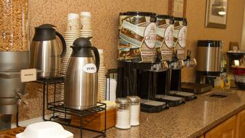 Un buffet de petit-déjeuner d’hôtel proposant divers distributeurs de café et de thé, un coin avec différents types de céréales et une machine à café.