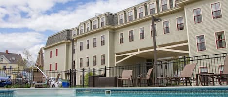 A hotel with a swimming pool, outdoor seating, and a covered patio area.