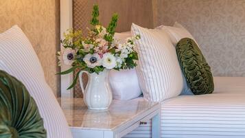 A neatly arranged bed with white linens and a decorative pillow, a white vase with flowers, and a textured green pillow.