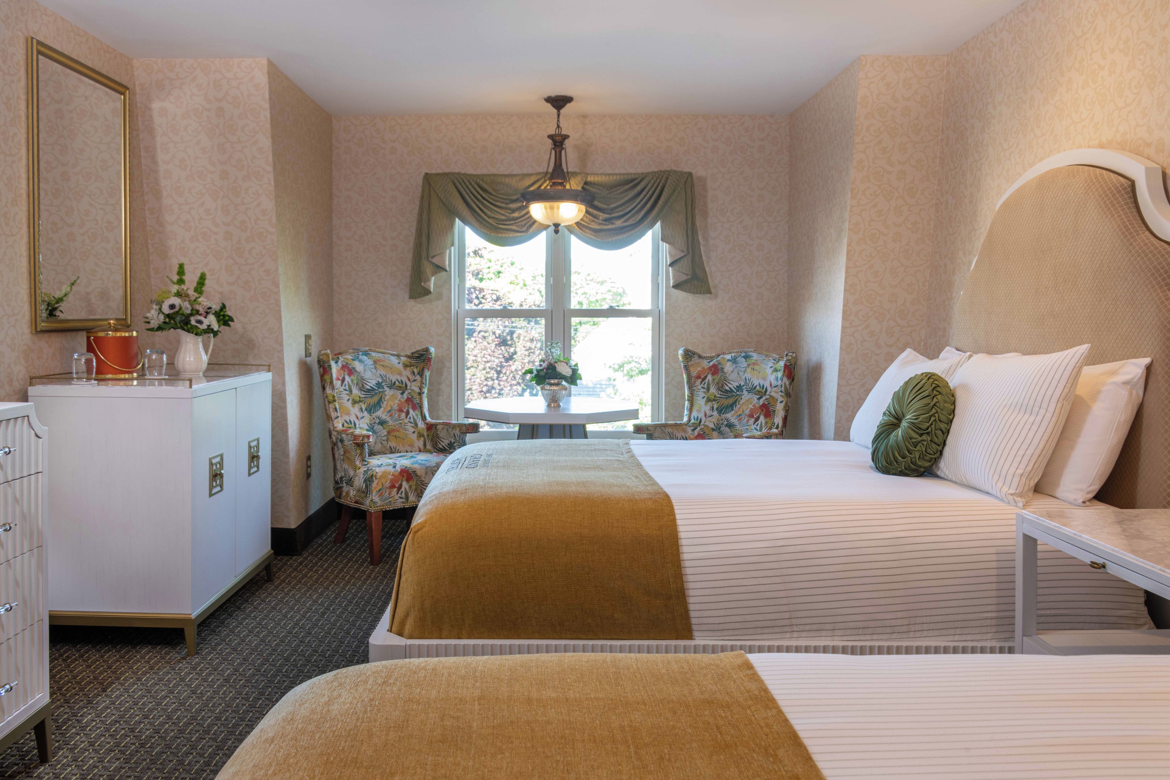 A hotel room with a bed, a desk, a chair, a dresser, and a window with curtains.