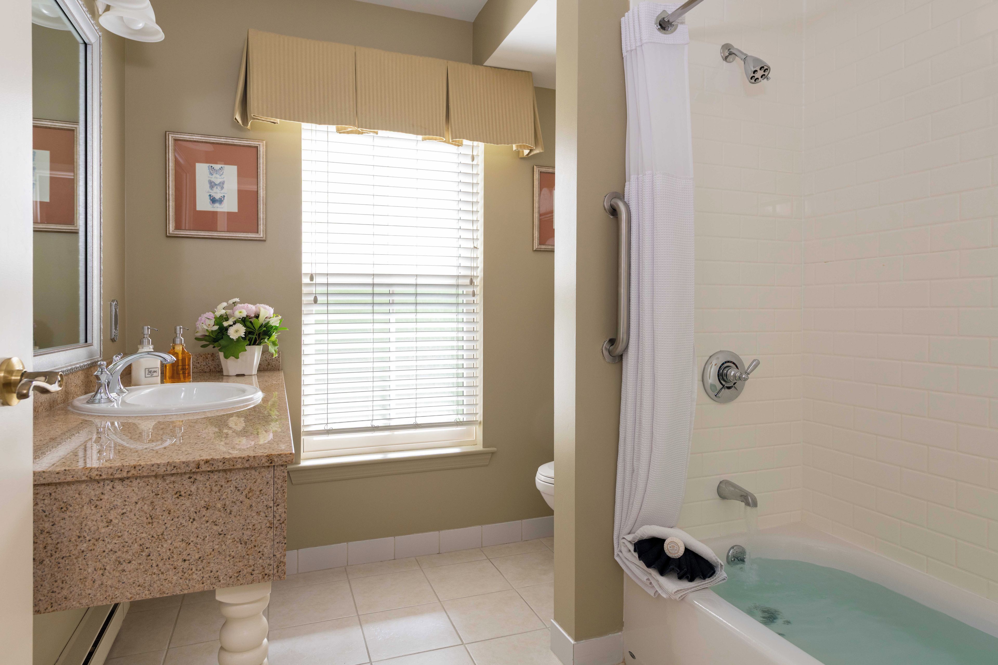 Un baño con bañera, lavamanos y ventana con persianas.