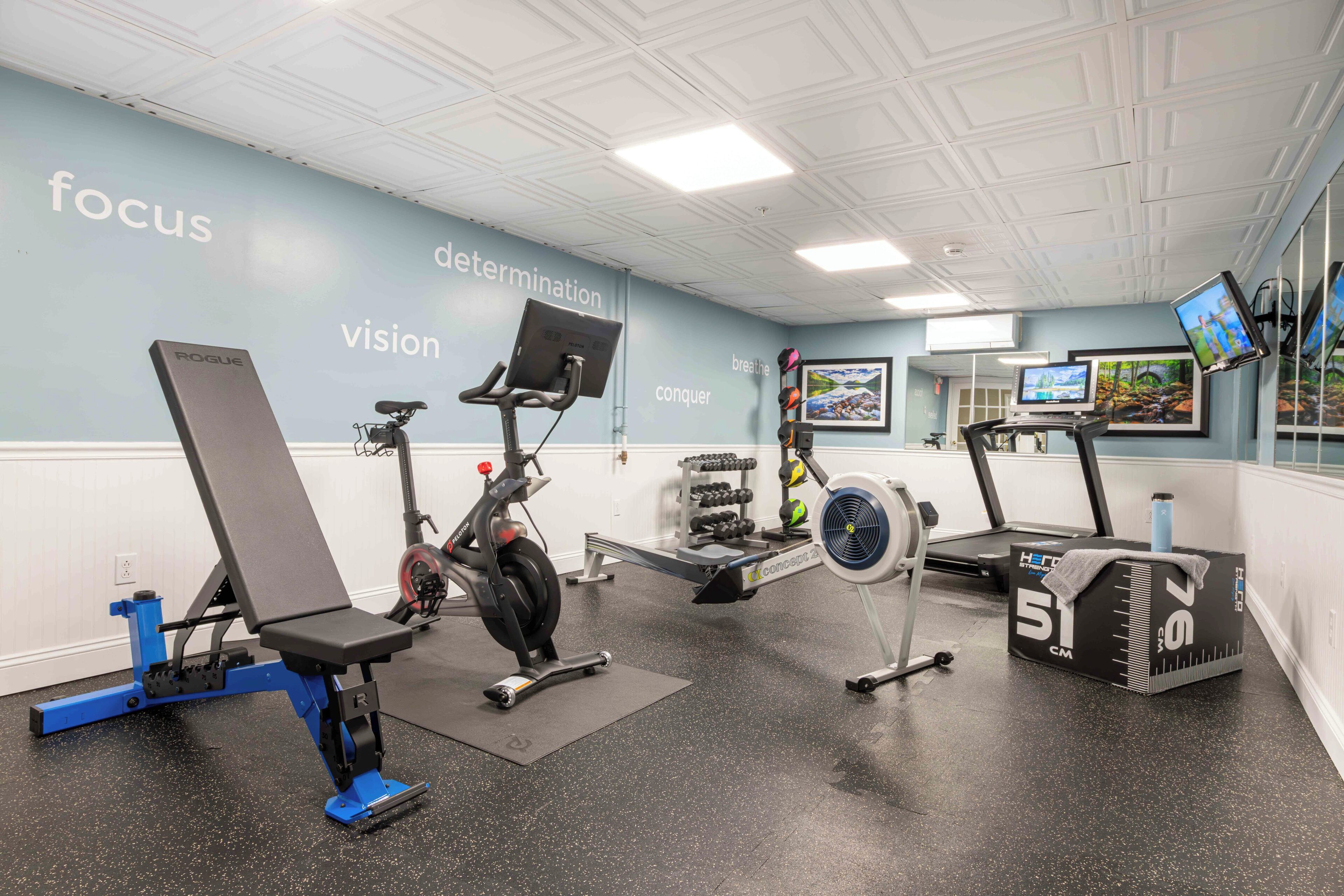 Ett gym med träningsutrustning, en vägg med motiverande ord och en spegel.