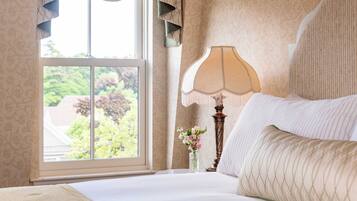 Een hotelkamer met een groot raam, een bed met witte lakens, een decoratieve lamp en een vaas met bloemen.