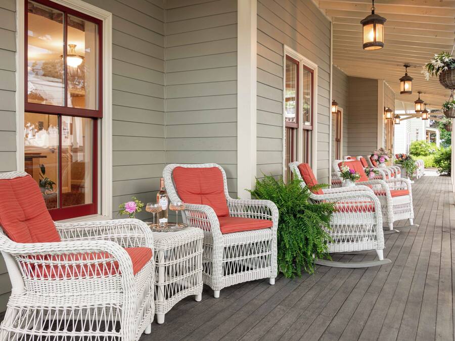 A covered outdoor seating area with wicker chairs and tables, a bottle of wine, and a tray.