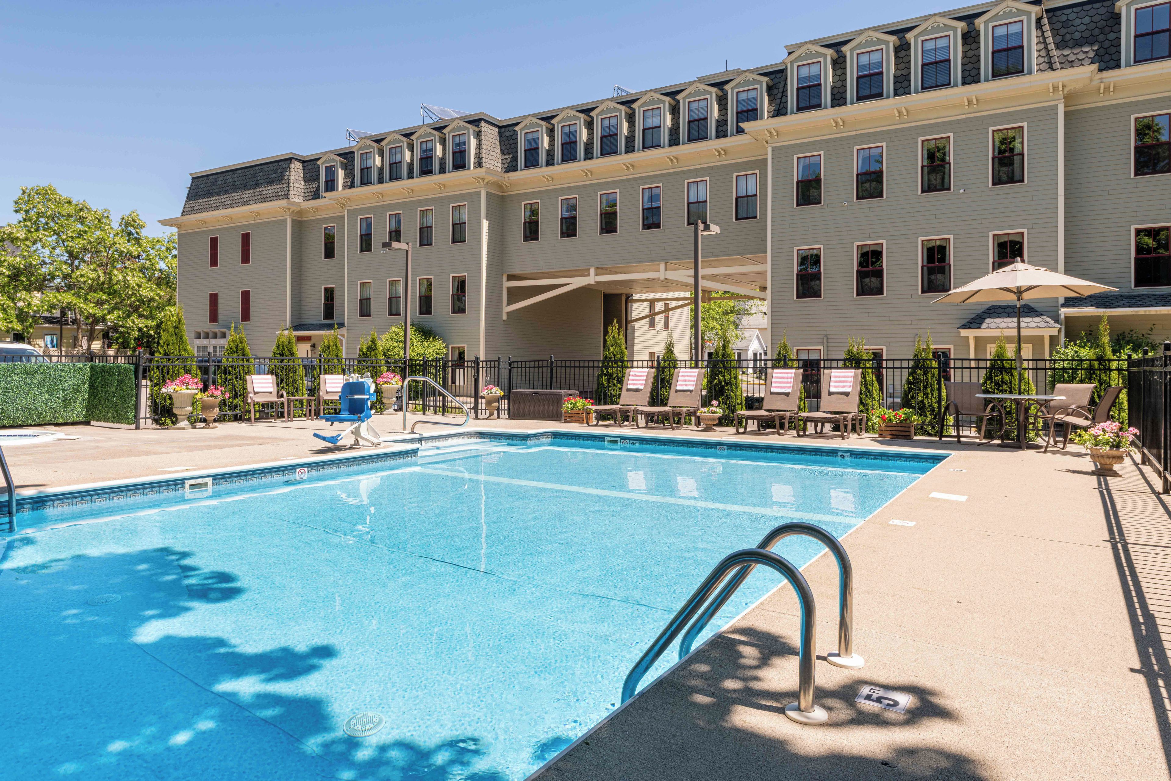 A swimming pool with a clear blue water surface, surrounded by lounge chairs and a covered seating area.