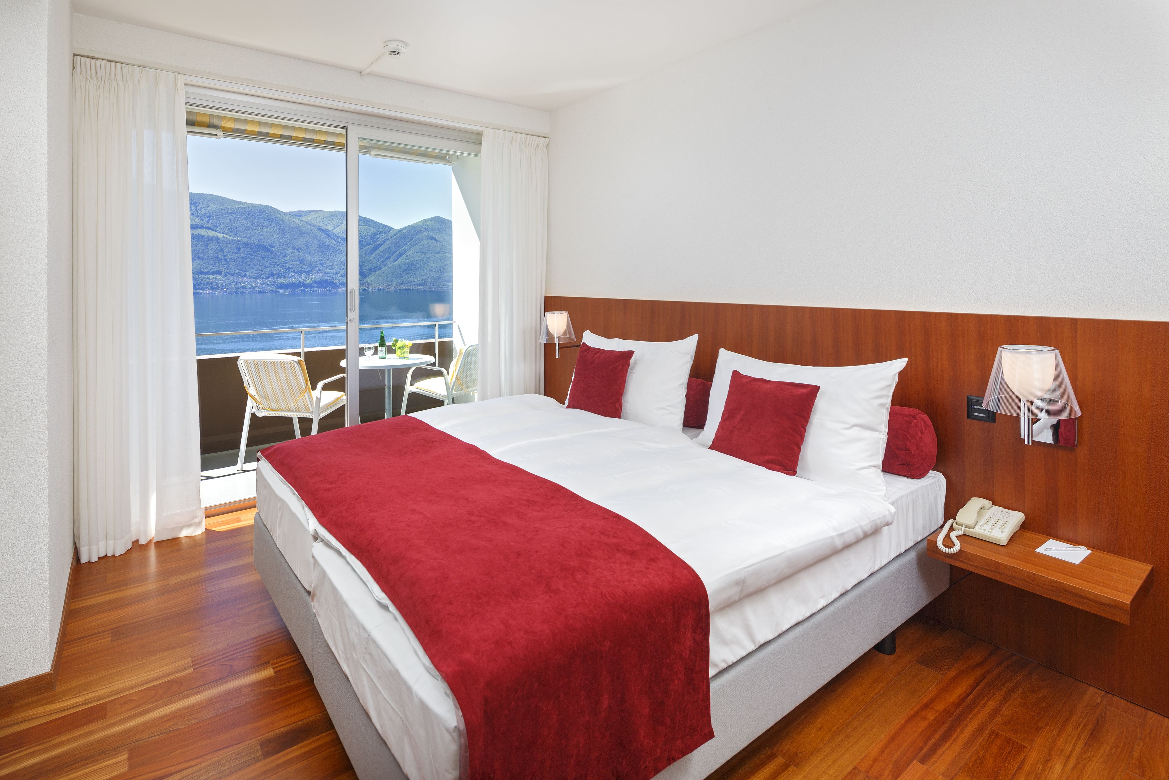A hotel room with a large bed, a bedside telephone, and a view of the mountains and water through the window.