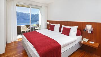 A hotel room with a large bed, a bedside telephone, and a view of the mountains and water through the window.