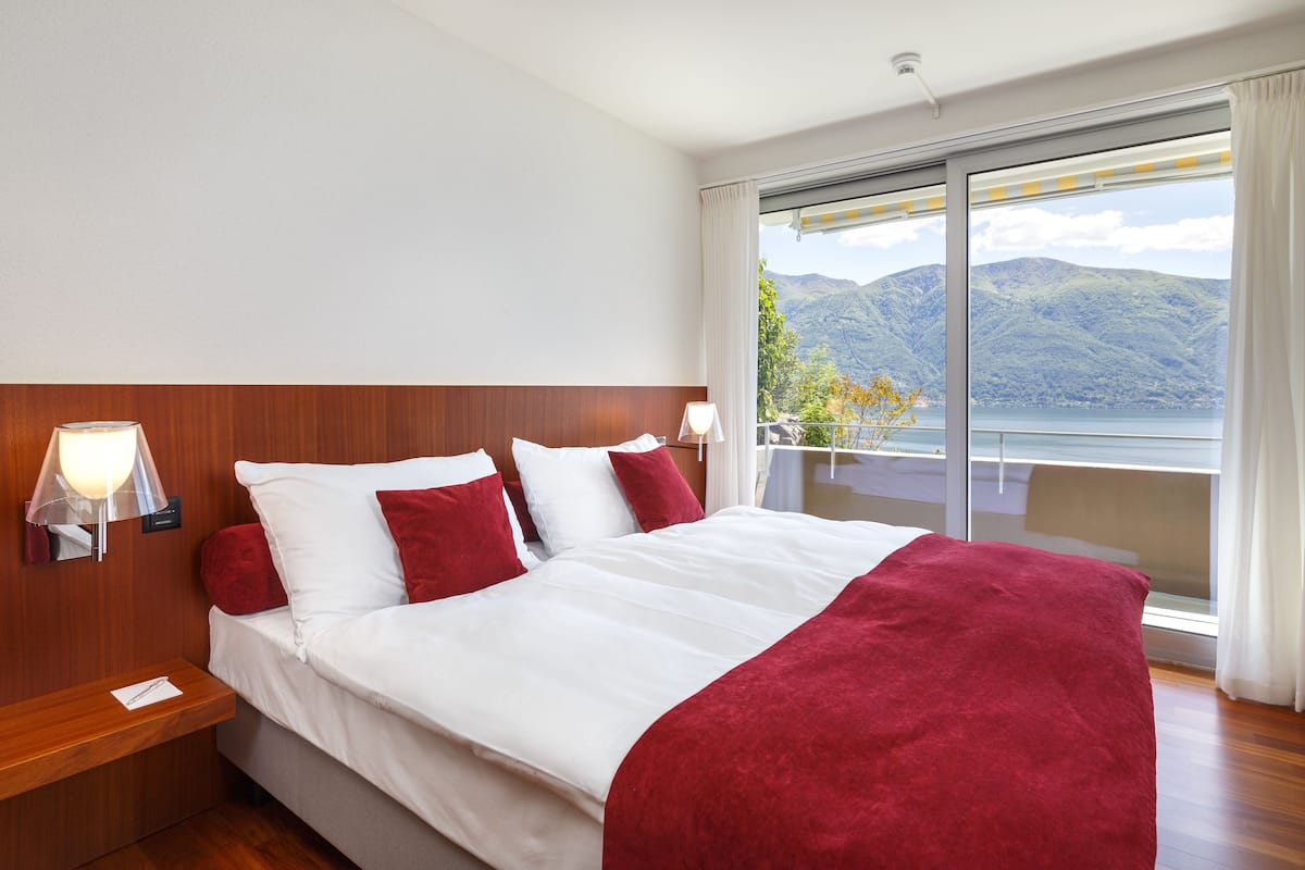 A hotel room with a large bed, two bedside tables, a nightstand, and a view of mountains through a sliding glass door.